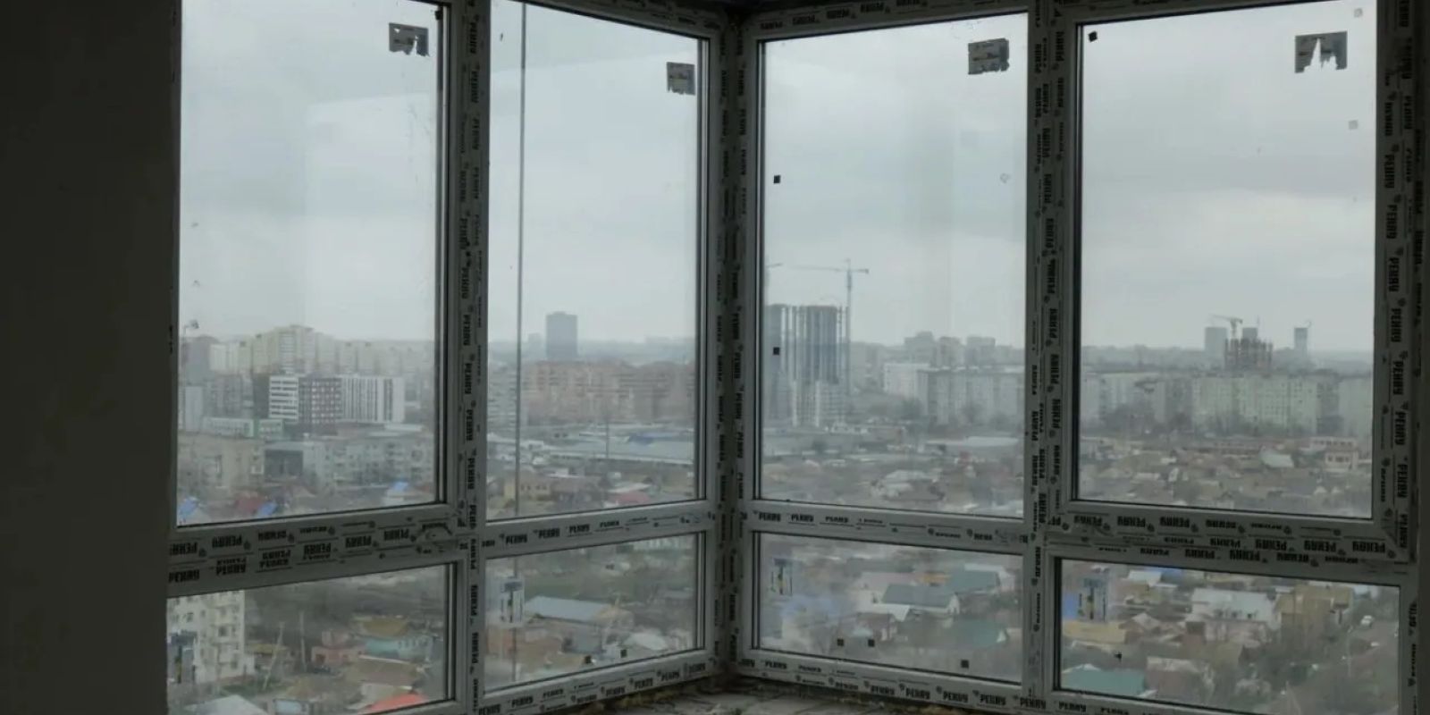 Угловое панорамное окно в новой квартире без отделки с видом на город